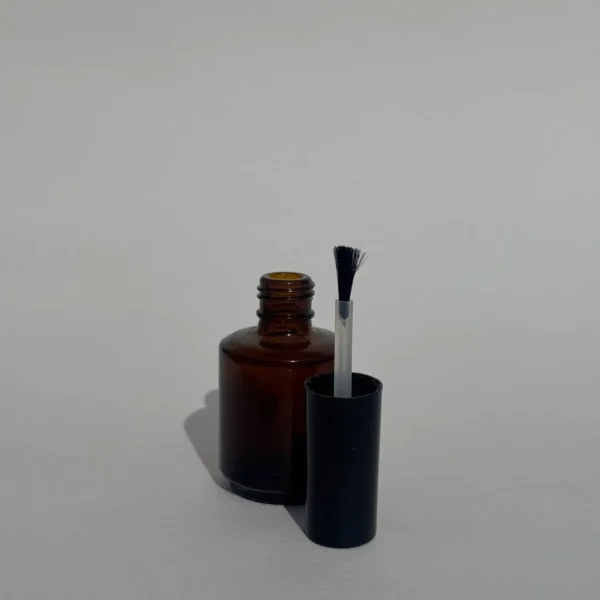 بطری شیشه‌ای لاک ۱۵ میلی‌لیتر شفاف با درب مشکی و فرچه، مناسب برای بسته‌بندی لاک‌های حرفه‌ای و محصولات مراقبتی ناخن