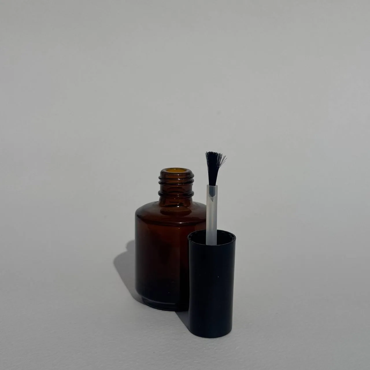 بطری شیشه‌ای لاک ۱۵ میلی‌لیتر شفاف با درب مشکی و فرچه، مناسب برای بسته‌بندی لاک‌های حرفه‌ای و محصولات مراقبتی ناخن